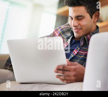 Trascorrere un po 'di tempo online. Girato di un bel giovane uomo usando il suo laptop mentre si rilassava sul divano a casa. Foto Stock