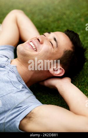 L'aria aperta porta un rinfrescante senso di calma. Scatto di un bel giovane uomo che si rilassa sull'erba all'aperto. Foto Stock