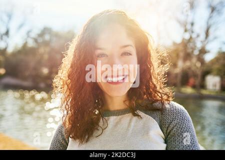 Il sole estivo è il motivo per cui amo l'aria aperta. Ritratto di una bella giovane donna in piedi accanto ad un lago. Foto Stock