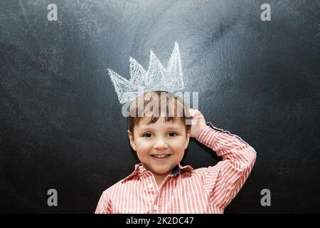 Disegnare è così divertente. Studio girato di un ragazzo adorabile con disegni in gesso dietro di lui. Foto Stock