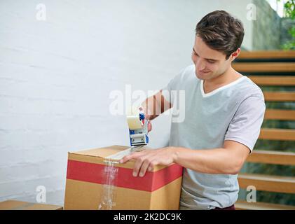 Sigillare le ultime scatole. Sparato di un giovane uomo che impacchettava i suoi effetti personali in scatole prima di uscire. Foto Stock