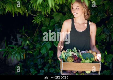 Mangiare meglio, sentirsi meglio. Una giovane donna che tiene una cassa di verdure all'aperto. Foto Stock