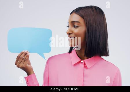 Im cercando il mio meglio per non ridere. Scatto di una giovane donna attraente che tiene bolla di discorso su uno sfondo grigio. Foto Stock