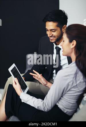 Hai fatto un ottimo lavoro qui. Scatto di due uomini d'affari che parlano insieme su un tablet digitale mentre si siedono in ufficio. Foto Stock