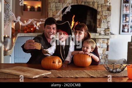 Questi momenti speciali meritano di essere catturati. Scatto di una famiglia giovane adorabile che prende selfie insieme con un cellulare su Halloween a casa. Foto Stock