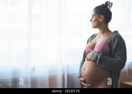 Il futuro sembra brillante per il suo nascituro bambino. Scatto corto di una giovane donna incinta attraente in piedi nella sua camera da letto a casa. Foto Stock