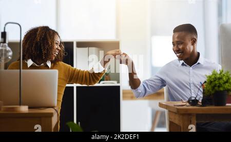 Portalo in partner. Scatto di due giovani colleghi di lavoro che si salutano con un pugno di pompa mentre si siedono in ufficio. Foto Stock