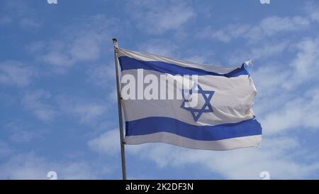 Bandiera israeliana che si intrecciano nel vento contro cieli luminosi Foto Stock