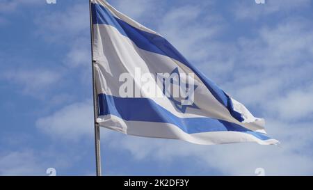 Bandiera israeliana che si intrecciano nel vento contro cieli luminosi Foto Stock