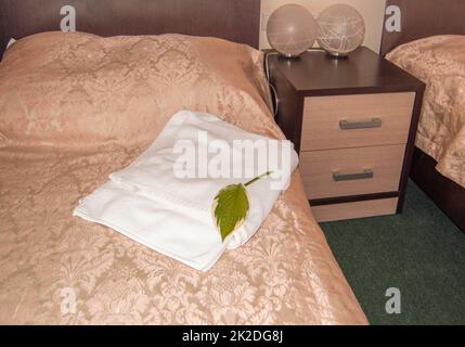 Gli interni di un hotel moderno, un letto con un cuscino e un lussuoso copriletto dorato e asciugamani bianchi, lampade di design sul comodino Foto Stock