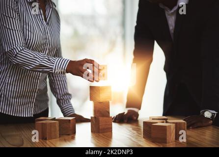 Il successo inizia costruendo una solida base. Sparato di due uomini d'affari impilando blocchi di legno insieme in un ufficio. Foto Stock