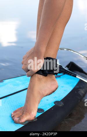 La donna sta fissando il guinzaglio da surf sulla caviglia Foto Stock