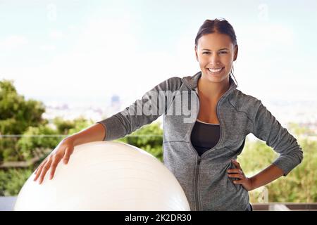 Pronto per una sessione di pilates stupefacente. Scatto corto di una giovane donna sportiva in piedi con una palla fitness. Foto Stock