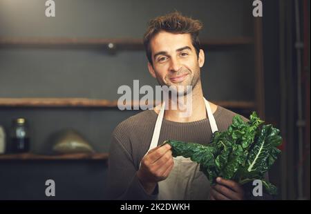 HES un ventilatore di spinaci. Scatto di un giovane che tiene un mazzo di spinaci nella sua cucina. Foto Stock