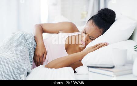 Non riesco a dormire anche attraverso questo dolore. Shot di una giovane donna attraente che soffre di crampi di stomaco mentre si trova nel suo letto a casa. Foto Stock