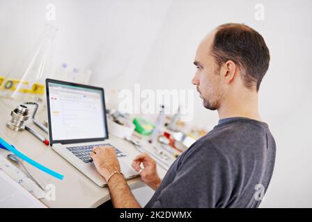 Perfezionare la sua nuova birra. Scatto di un uomo che lavora su un computer portatile mentre è circondato da attrezzature per la preparazione del caffè. Foto Stock