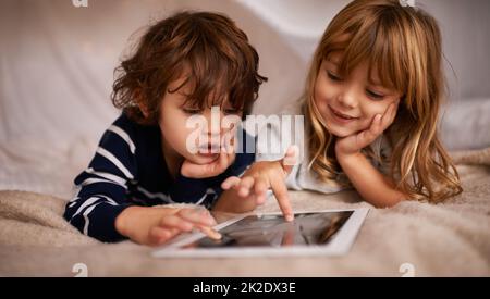 Boardgames è diventato digitale. Scatto di due adorabili fratelli utilizzando un tablet digitale mentre si trova su un letto. Foto Stock