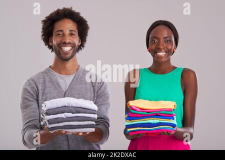 Parità di genere. Studio girato di un giovane uomo e una donna, ognuno con un mucchio di vestiti ben piegato. Foto Stock