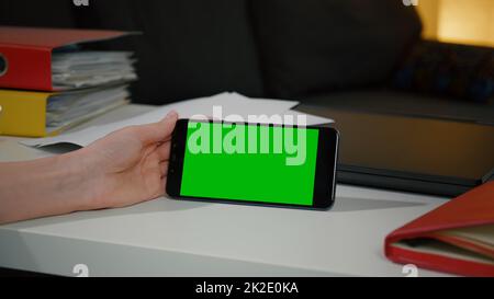 Donna che guarda il telefono smartphone con schermo verde chroma display chiave seduto alla scrivania. Foto Stock