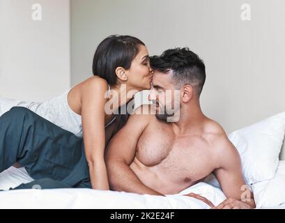 Iniziare la giornata con un bacio fresco. Scatto corto di una giovane coppia sposata affettuosa a letto a casa. Foto Stock