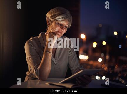 Pensare a un job Bravo. Scatto corto di una donna d'affari matura attraente usando il suo tablet mentre lavora tardi in ufficio. Foto Stock