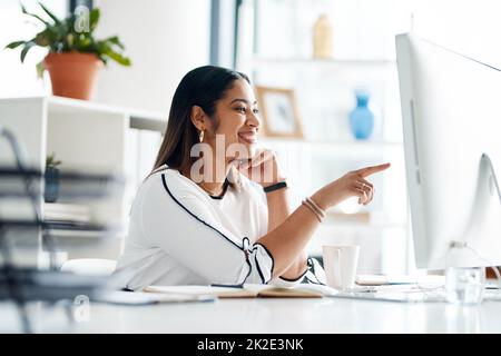 Sembra che abbia trovato qualcosa di utile. Scatto di una giovane donna d'affari che lavora su un computer in un ufficio. Foto Stock