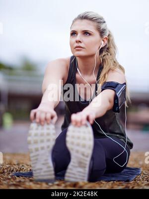 Entrare nella zona con una grande musica. Scatto di una giovane donna che allunga le gambe prima di una corsa. Foto Stock