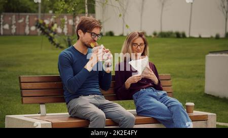 Giovani uomini d'affari che hanno uno spuntino con cibo da asporto in un parco. Mangiare all'aperto. Gustare il cibo. Odore di buoni spuntini. Foto Stock