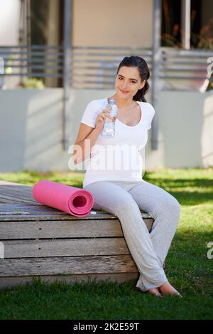 Dopo un allenamento di yoga, ti sentirai ristorato. Shot di una giovane donna incinta seduta con il suo tappeto yoga all'esterno. Foto Stock