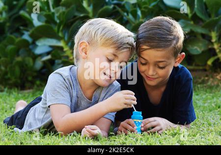 Resta selvaggio, youll ottenere più vecchio, per favore non crescere. Colpo di due adorabili ragazzi che giocano con le bolle sull'erba nel cortile. Foto Stock