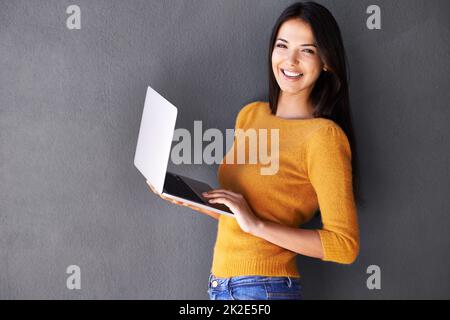 Shes una farfalla sociale online. Ritratto di una bella giovane donna utilizzando un portatile su sfondo grigio. Foto Stock