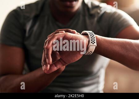 Inoltre, tiene traccia della velocità e della distanza percorsa. Scatto corto di un uomo irriconoscibile che controlla il suo orologio da polso. Foto Stock