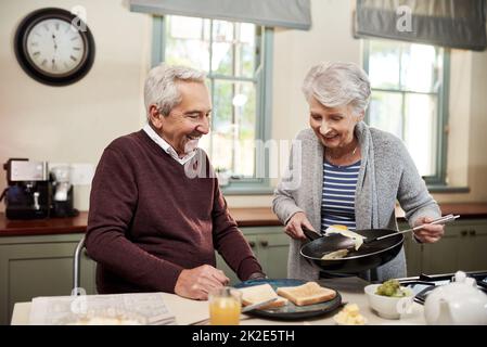 Viene servita la prima colazione. Shot di una coppia affettuosa senior che cucinano insieme nella loro cucina a casa. Foto Stock