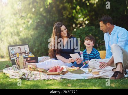 Pranzare all'aperto è fantastico. Scatto di una giovane famiglia utilizzando un tablet digitale durante un picnic nel parco. Foto Stock