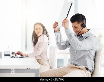 Questa cosa darn non funzionerà. Scatto di un giovane agente del call center che distruggesse un laptop mentre lavora in ufficio. Foto Stock