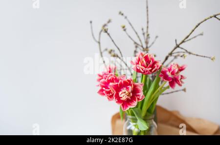 Un bel bouquet primaverile di tulipani si erge in un vaso insieme ai rami primaverili. Concetto di sorpresa, compleanno. Luogo per un'iscrizione. Foto Stock