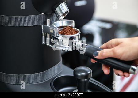 Il barista macina i chicchi di caffè nel portafiltro Foto Stock