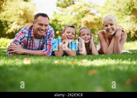 Questi sono i momenti che contano nella vita.... Un ritratto della vista frontale di una famiglia felice che si trova sull'erba all'aperto. Foto Stock