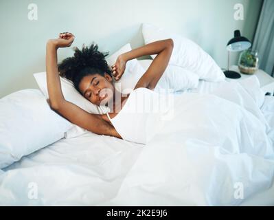 Sentirsi ben riposati e pronti per la giornata. Scatto di una giovane bella donna svegliarsi e stretching nel suo letto a casa. Foto Stock
