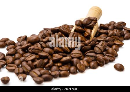 Mucchio di chicchi di caffè tostati con paletta in legno su sfondo bianco, messa a fuoco selettiva. Foto Stock