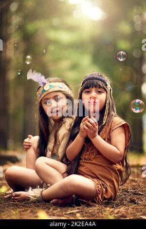 Questo è il modo in cui inviamo segnali di fumo. Scatto di due bambini giovani che soffiano bolle mentre giocano dressup nei boschi. Foto Stock