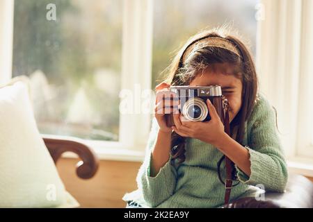 Chissà dove il suo hobby potrebbe guidarla. Scatto di una bambina che scatta foto con una macchina fotografica vintage a casa. Foto Stock