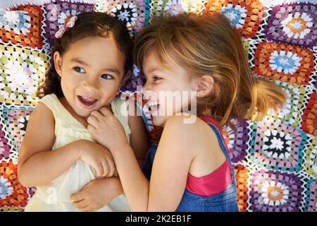 Infanzia firendship. Colpo ad angolo alto di due bambine che si stendono giù e giocano su una coperta. Foto Stock