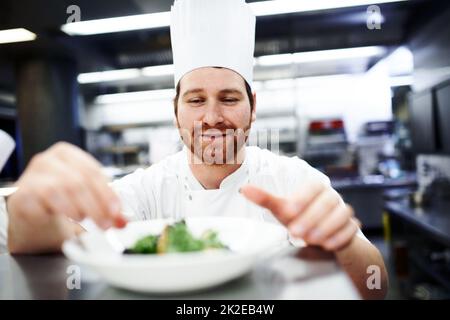 Mettendo sui ritocchi di finitura. Shot di uno chef che mette i tocchi finali su un piatto da pranzo in una cucina professionale. Foto Stock