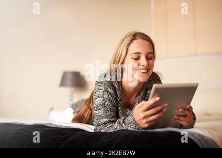 Collegandosi dalla comodità del suo letto. Scatto corto di una giovane donna attraente utilizzando un tablet digitale a casa. Foto Stock