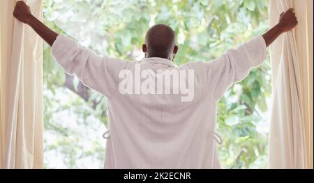 Iniziamo questa giornata. Scatto di un giovane uomo che apre le tende a casa. Foto Stock