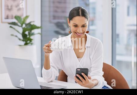 Quando il nostro sole è aumentato, avete scelto l'ombra. Scatto di una donna d'affari che usa il suo cellulare mentre godendo una pausa caffè in un ufficio moderno. Foto Stock