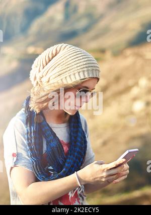 Collegato nella natura selvaggia. Scatto ritagliato di una ragazza adolescente che invia un messaggio di testo all'aperto. Foto Stock
