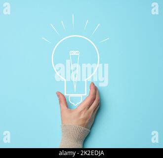 La mano della donna e una lampada elettrica disegnata su uno sfondo blu. Il concetto di ricerca di idee e soluzioni, brainstorming. Passando a forme alternative di energia Foto Stock