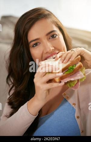 Così tanto di yumminess. Shot di una giovane donna che prende un boccone da un panino. Foto Stock